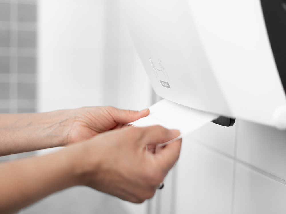 Person tar papper ur en Katrin System Towel dispenser White