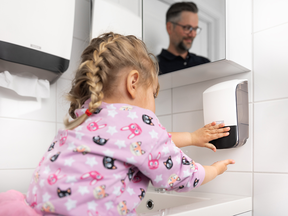 Flicka tar tvål ur en Katrin Soap Dispenser 500 ml